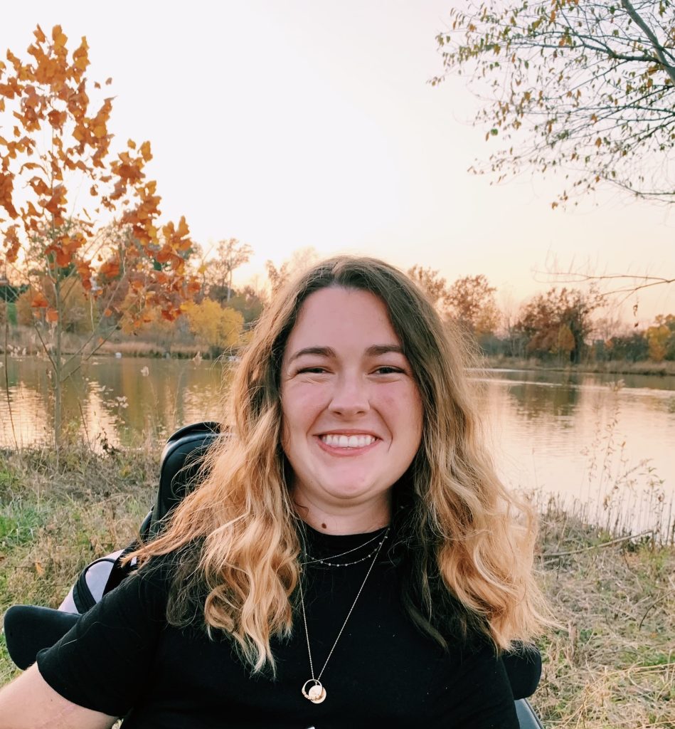 Ellie Stitzer, a young white woman with long blonde hair, is smiling in front of a body of water.